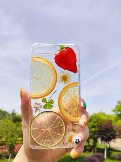Transparent iPhone case featuring dried flowers, a strawberry, and citrus slices — lemon and lime, with green clover.