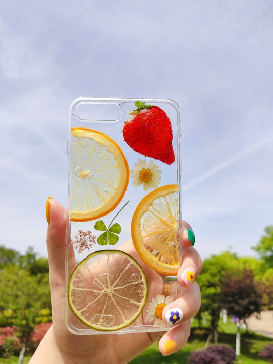 Transparent iPhone case featuring dried flowers, a strawberry, and citrus slices — lemon and lime, with green clover.