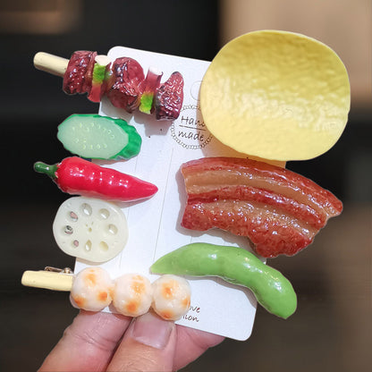 Resin food hair clips held in a hand: potato chip, bacon, red chilli, skewers and cucumber
