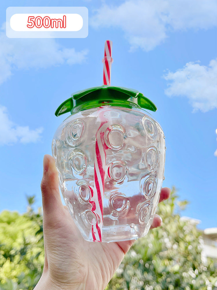 Hand holding strawberry-shaped 500ml cup with green leaf lid and red-white striped straw against blue sky.