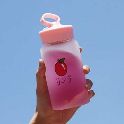 Hand holding one frosted pink ombre bottle with loop cap, red fruit icon and Japanese text.
