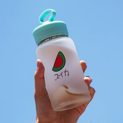 Hand holding one frosted white bottle with a mint-green loop lid, watermelon slice graphic and Japanese text.