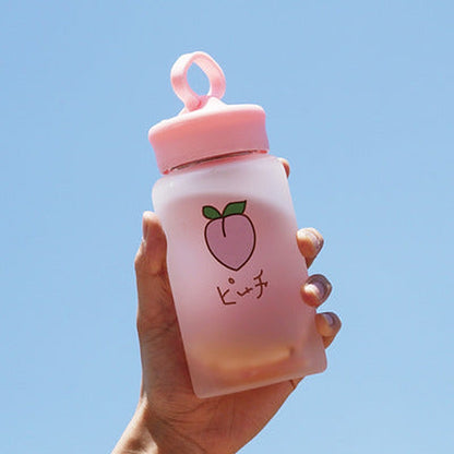 Hand holding one frosted pink bottle with loop cap, peach illustration and Japanese text against blue sky.