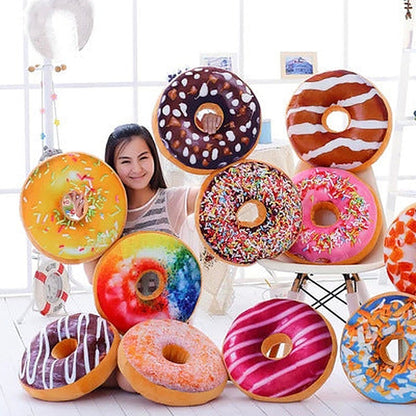 11 large colourful donut plush pillows with assorted frostings and sprinkles around a seated woman.
