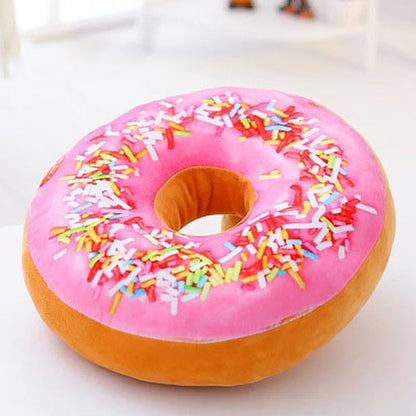 One round donut-shaped plush pillow with pink frosting, multicoloured sprinkles and tan base.