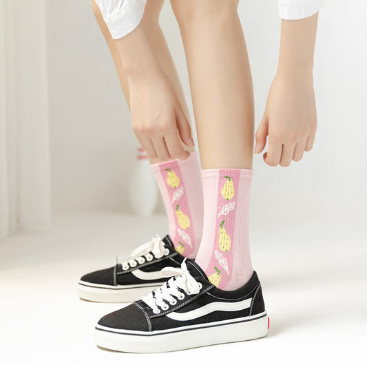 Two pink crew socks with yellow pineapples worn with black canvas sneakers with white stripe.