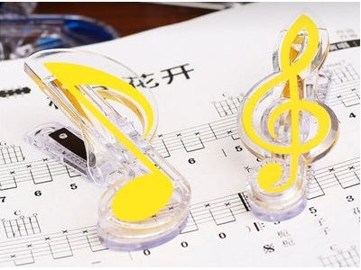Two clear plastic bag clips shaped like a musical note and treble clef with yellow insets on sheet music.