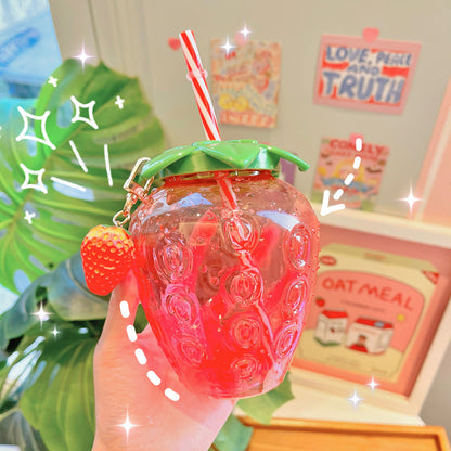 One translucent red-pink strawberry-shaped water bottle with green leaf lid, striped straw and strawberry c...