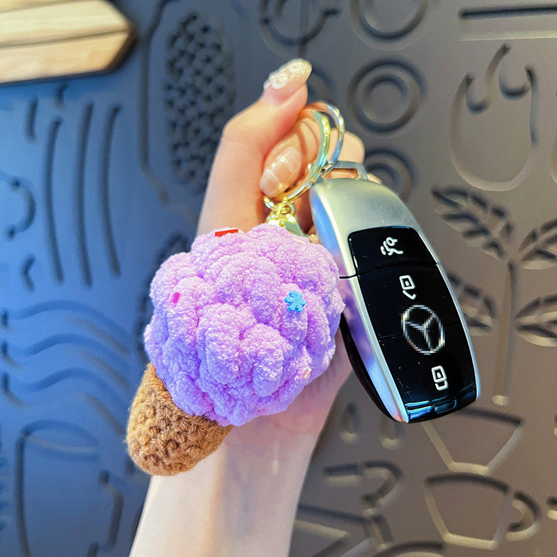 Hand holding gold keyring with Mercedes key fob and one purple plush ice cream cone keychain (brown cone).