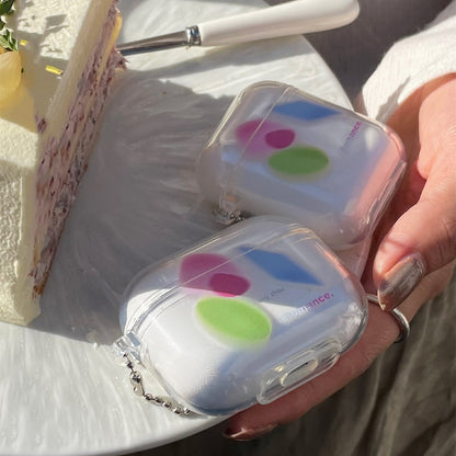 Two clear AirPods cases with white inserts showing pink, green and blue spots and a small silver ball chain.
