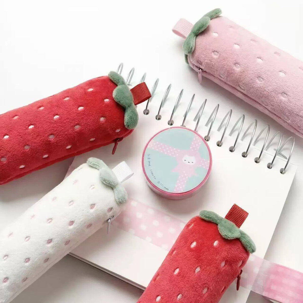 Strawberry plush pencil cases on a notebook