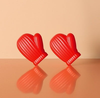 Two red mitten-shaped plastic clips with ribbed texture, tilted on a reflective peach surface.