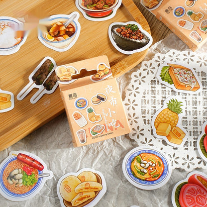 One small beige sticker box and about 11 colorful food stickers (bowls, pineapple, skewers) on wood and doily.