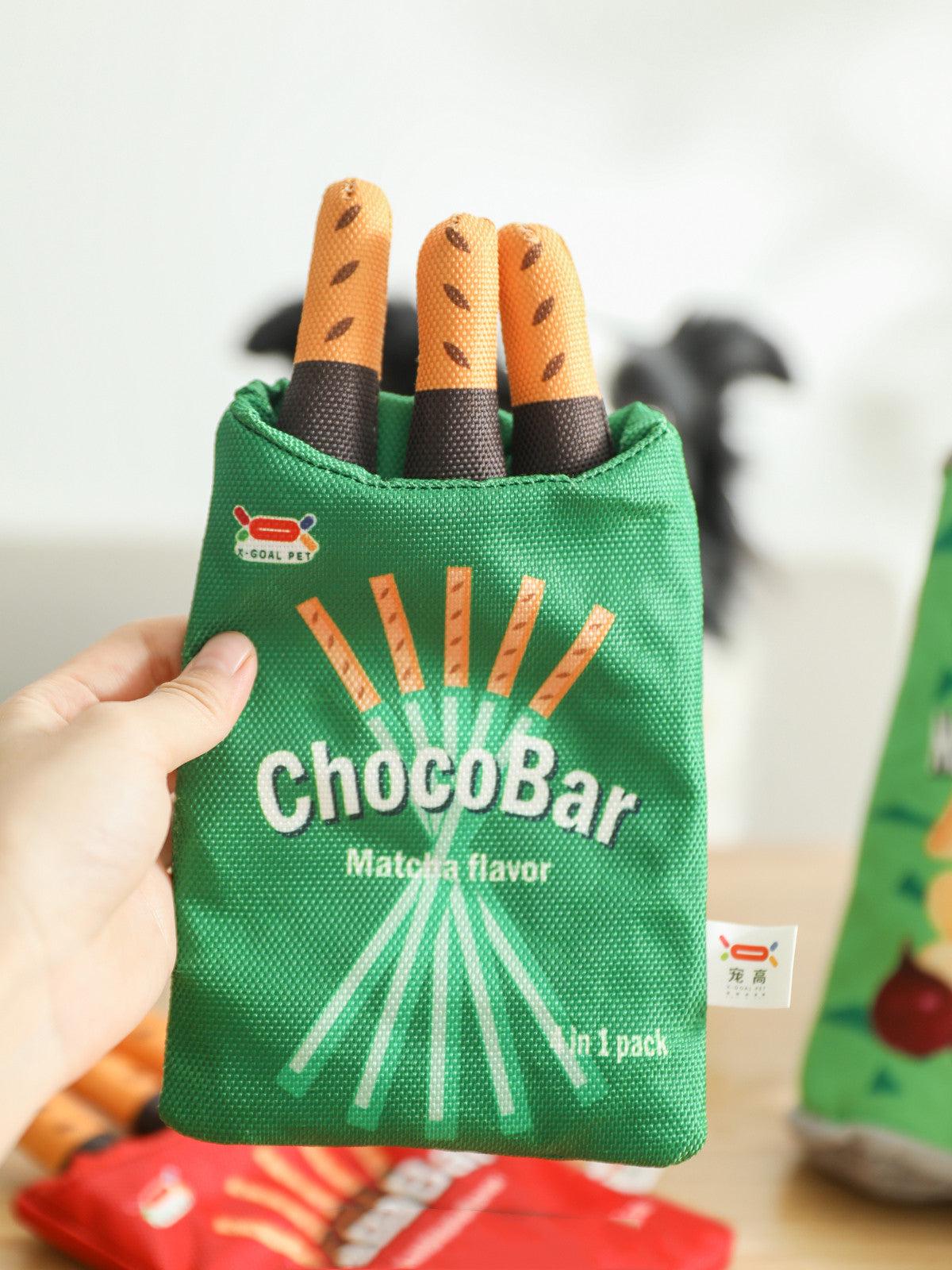Hand holds green fabric pouch labeled ChocoBar Matcha flavor with three orange-brown plush sticks.
