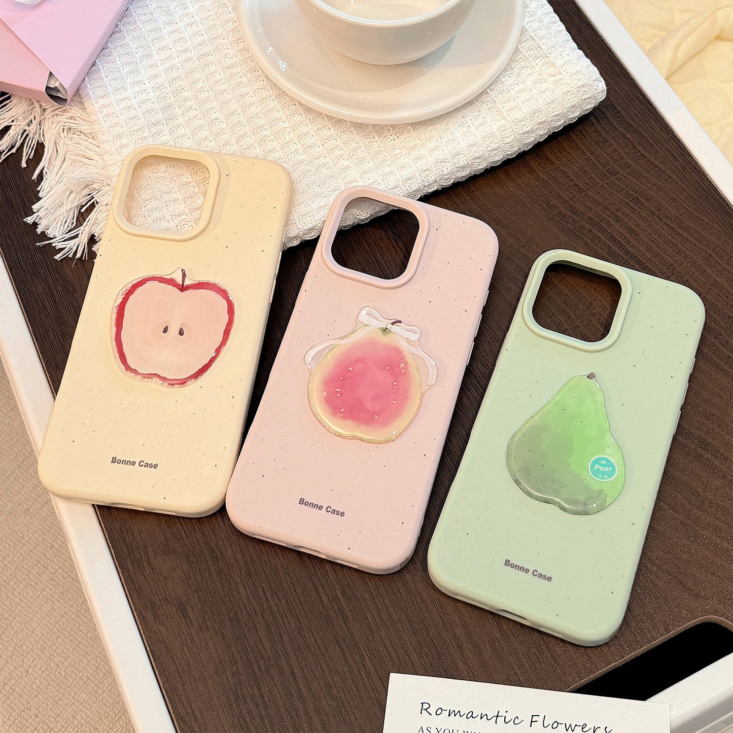 Three 3D fruit silicone iPhone cases in pale pink, green, and cream, featuring apple, pear, and peach designs.