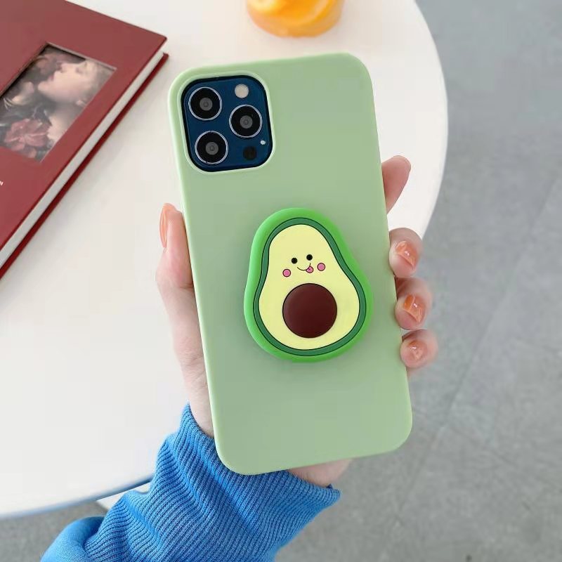 Hand holding one light-green iPhone case with an attached avocado-shaped phone grip showing a smiling face.