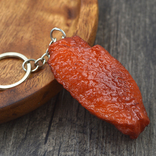One realistic-looking reddish-brown textured chicken wing keychain with silver ring on a wooden board.