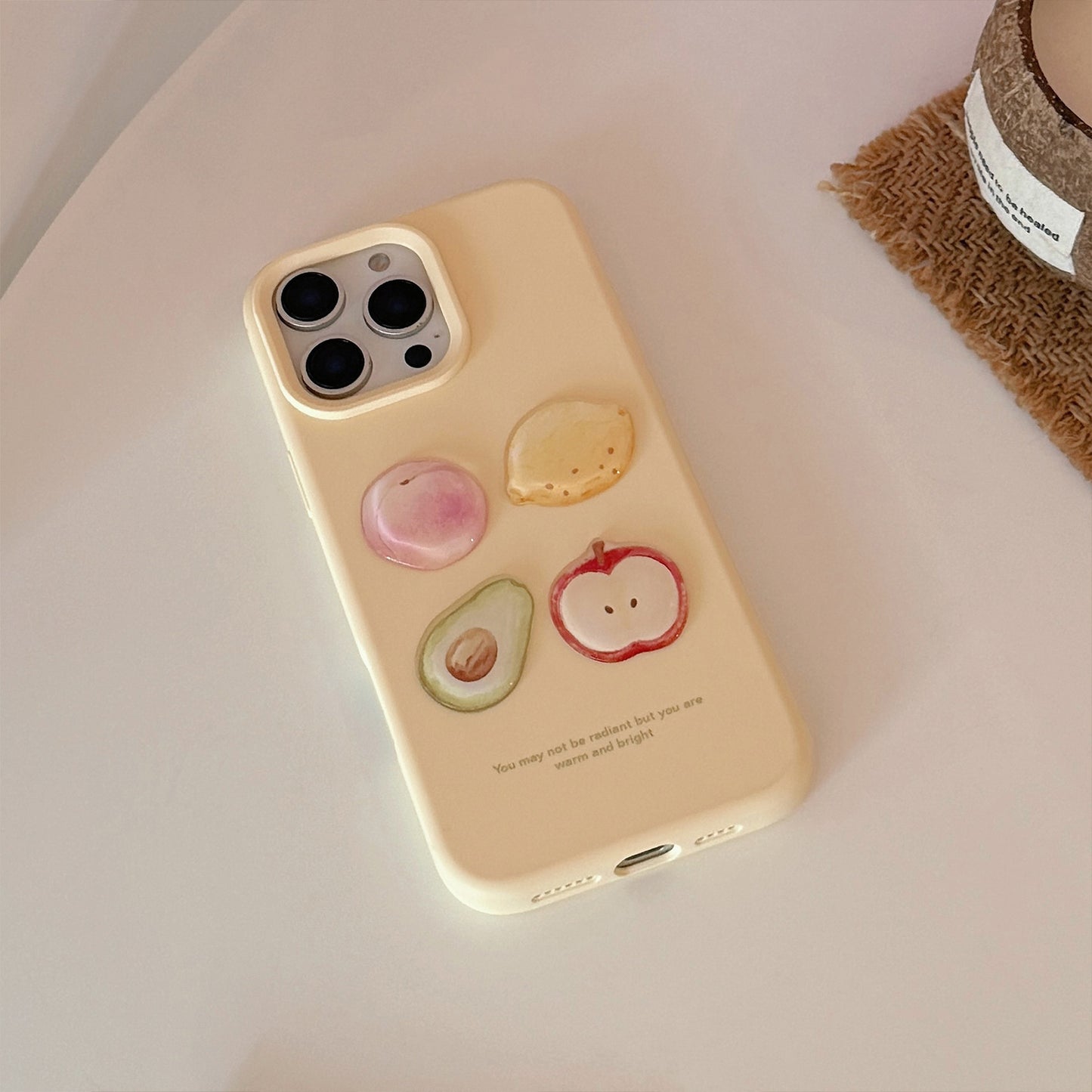 Cream iPhone case featuring 3D fruit designs: peach, avocado, apple, and lemon in vibrant colours.