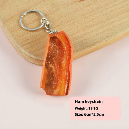 Single glossy orange-brown ham-shaped keychain with silver split ring on wood board and pink background.