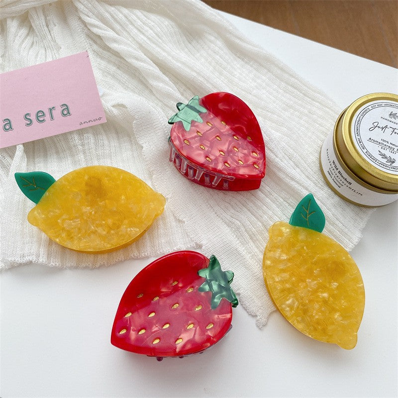 Four fruit-shaped hair claws: two red strawberry clips with green tops and two marbled yellow lemon clips.
