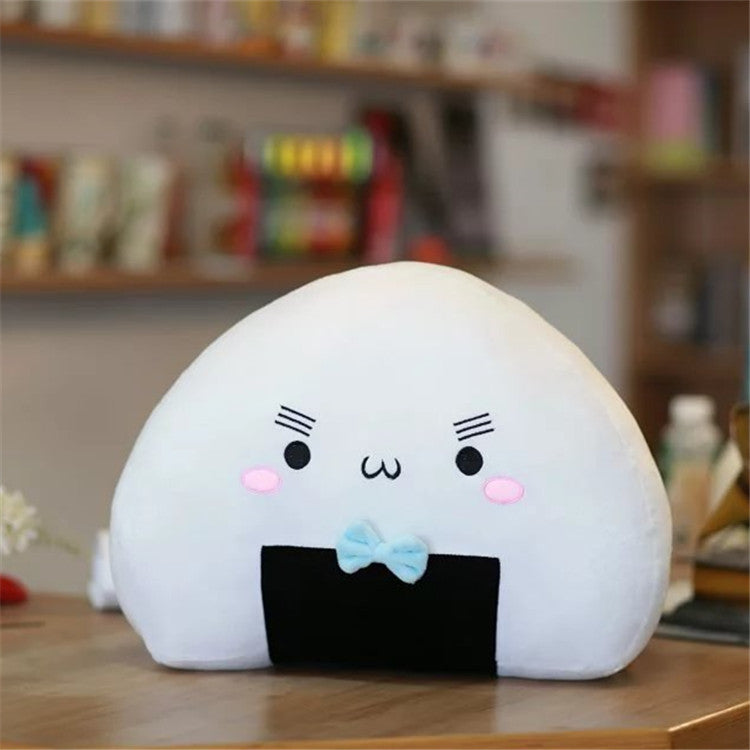 Single white triangular plush pillow with kawaii face, black bottom patch and light blue bow on wooden table.