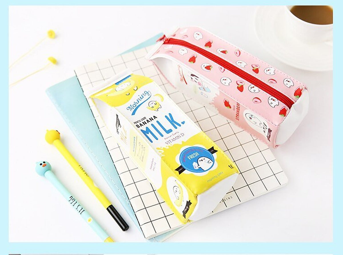 Pink strawberry and yellow banana milk carton pencil cases lying on a grid notebook with gel pens