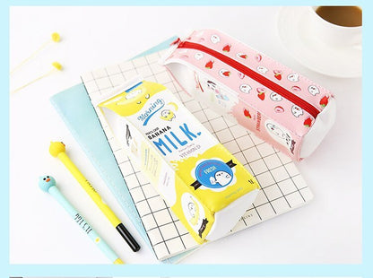 Pink strawberry and yellow banana milk carton pencil cases lying on a grid notebook with gel pens
