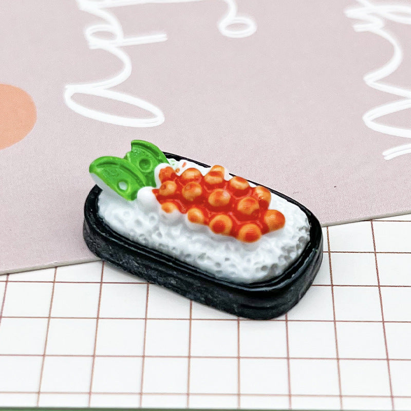 One miniature sushi piece with black rectangular base, textured white rice, orange roe and two green leaves.