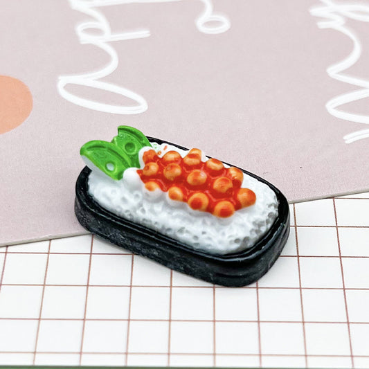 One miniature sushi piece with black rectangular base, textured white rice, orange roe and two green leaves.