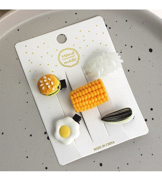 Card of five food hair clips: burger, corn, fried egg, rice and sunflower seed