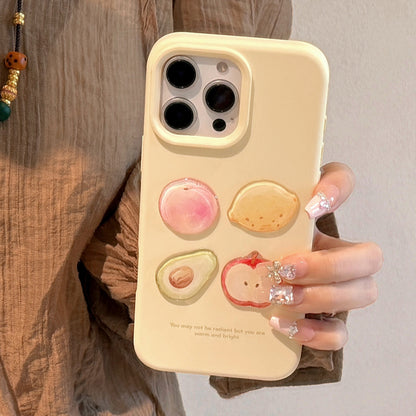 Yellow iPhone case featuring 3D fruit designs: avocado, apple, lemon, and peach, with a warm quote at the bottom.