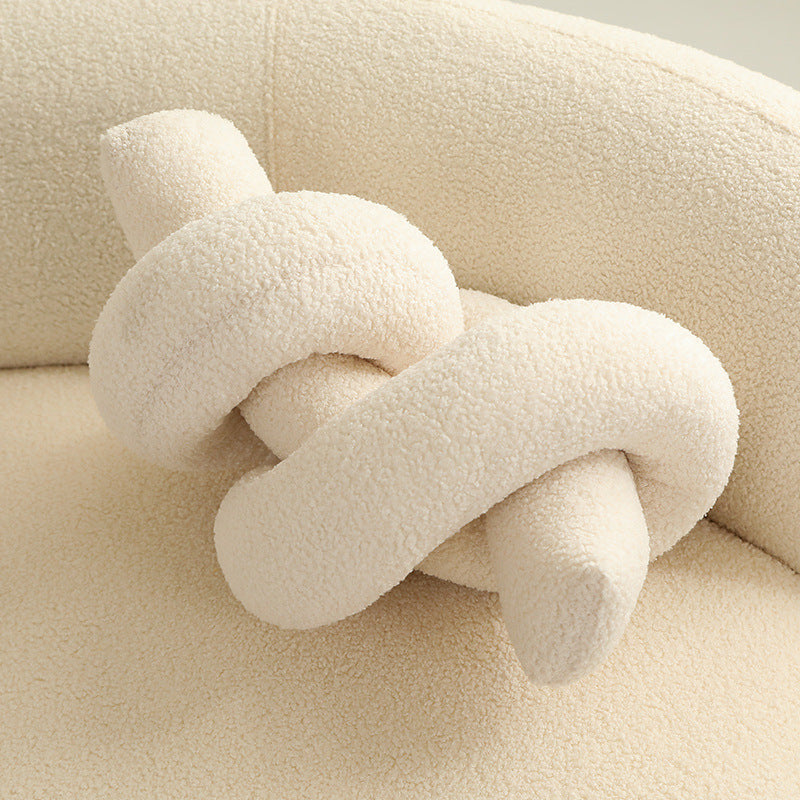 One cream-colored knotted tubular cushion with boucle texture on a matching sofa.