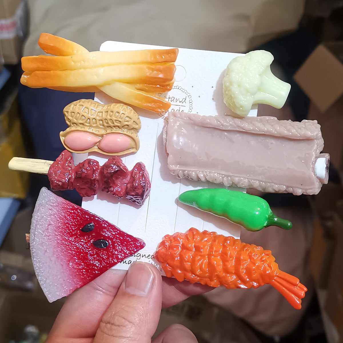 Resin food hair clips held in a hand: french fries, peanut, pork rib, watermelon, chilli and prawn