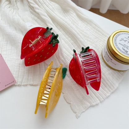 Three fruit-shaped hair claw clips: two red strawberry clips with green leaves and one yellow lemon clip.