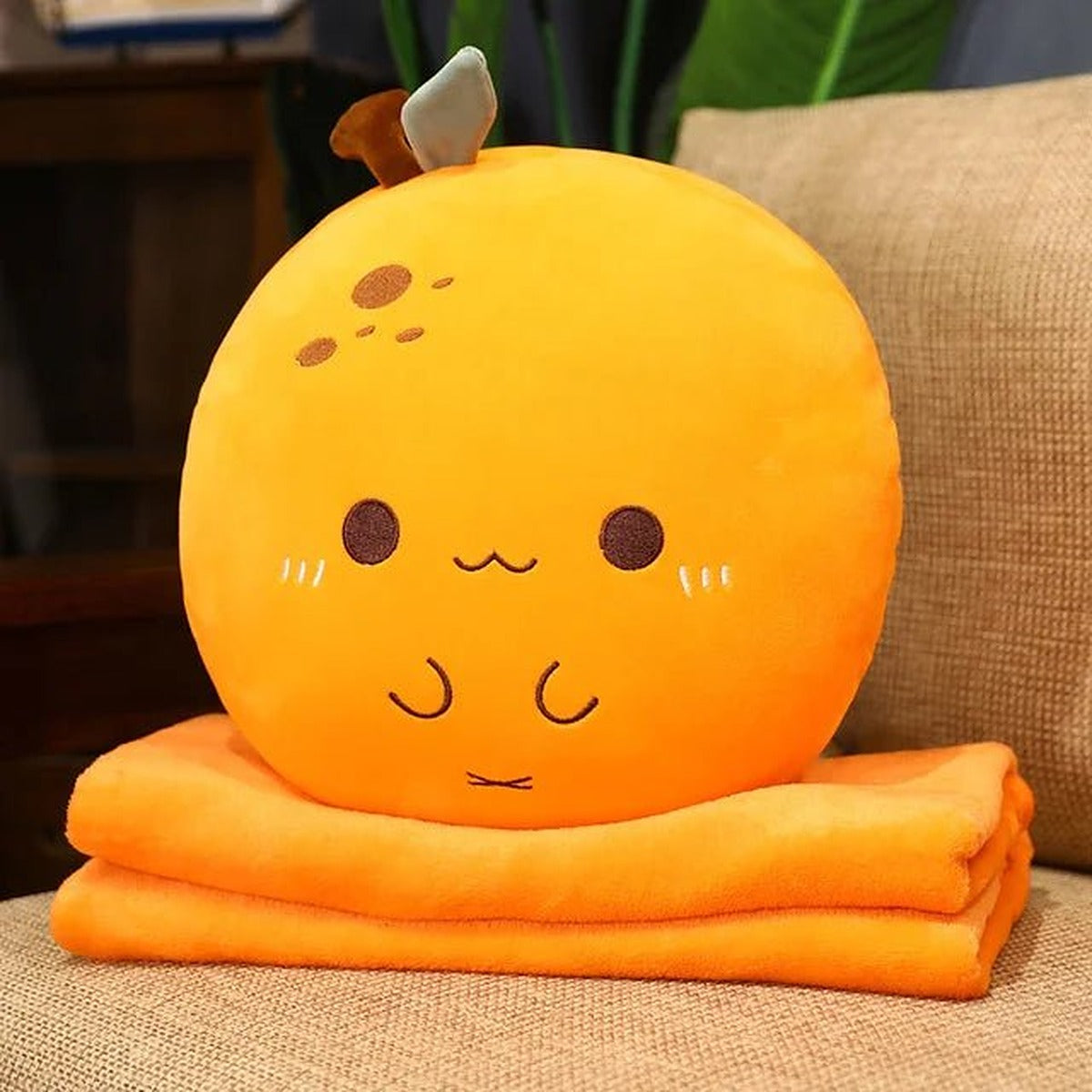 Orange plush pillow sitting on its folded orange blanket