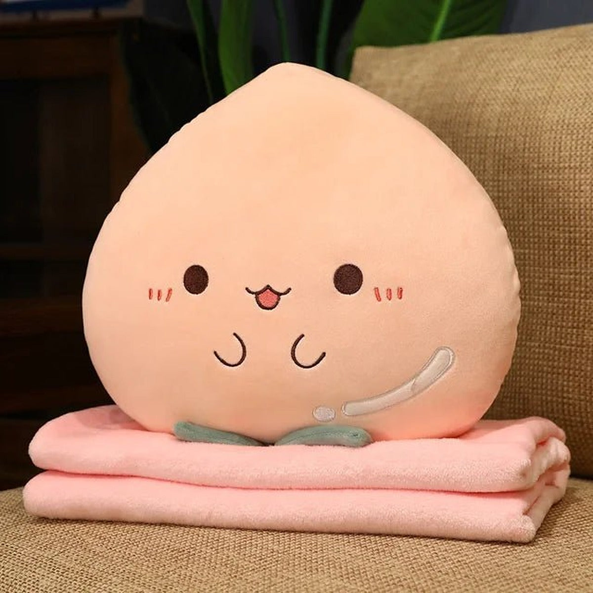 Peach plush pillow sitting on its folded pink blanket