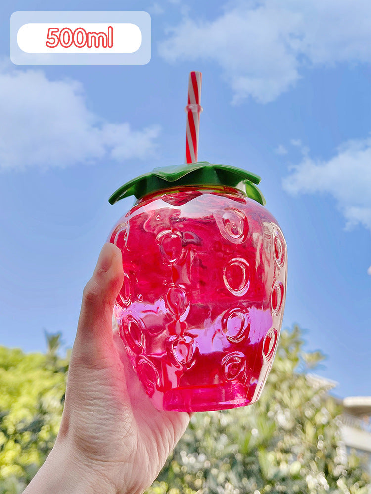 Hand holds one translucent pink strawberry 500ml bottle with green lid and red-white straw against blue sky.