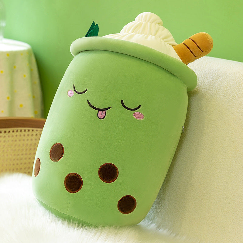 One green cup-shaped plush pillow with whipped-cream top, brown boba dots, smiling closed eyes and tongue.