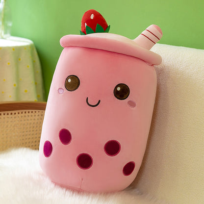 Pink plush milk-tea cup pillow with smiling face, brown eyes, five dark boba dots and strawberry-topped lid.