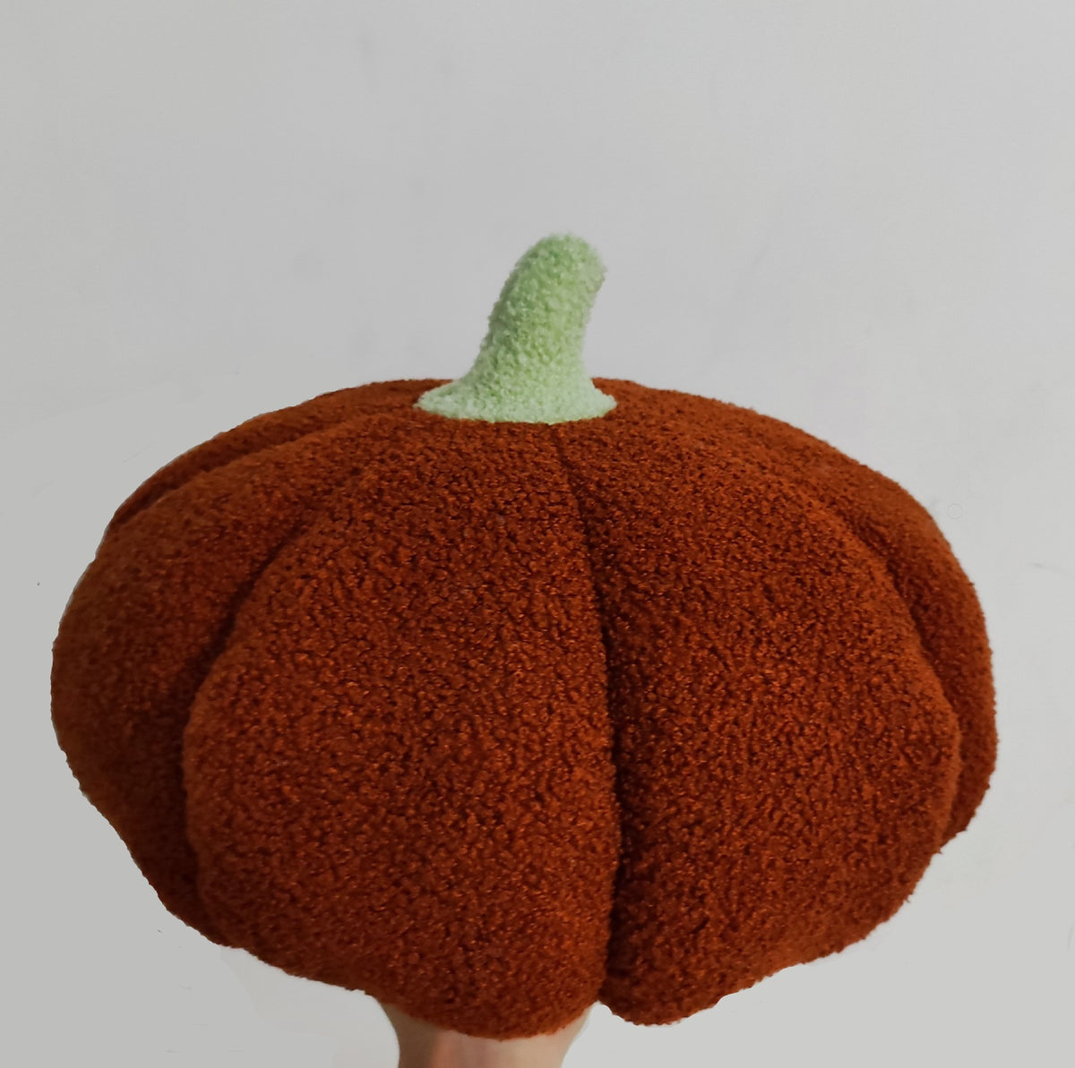 Chestnut brown teddy pumpkin plush cushion with a pale green stem held up by a hand