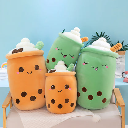 Four plush bubble-tea pillows, two orange and two green, with faces, white cream tops, straws and brown boba.