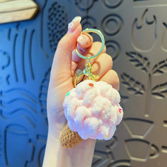 Hand holding one plush pink ice cream cone keychain with gold ring, brown knit cone and sequin sprinkles.