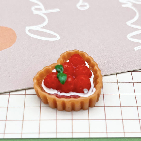 One heart-shaped tan tart with red berry topping, white cream rim and small green leaf.