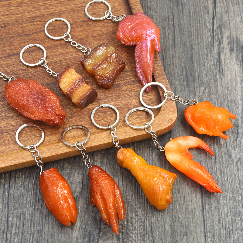 Ten glossy meat-shaped keychains with metal rings on a wooden board and gray wood surface.