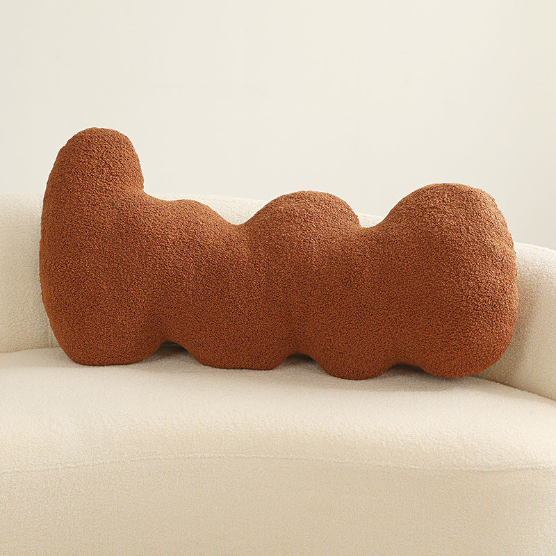 One rust-coloured boucle cushion with three rounded lobes placed on a cream sofa.