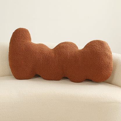 One rust-colored boucle cushion with three rounded lobes placed on a cream sofa.