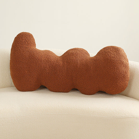 One rust-coloured boucle cushion with three rounded lobes placed on a cream sofa.
