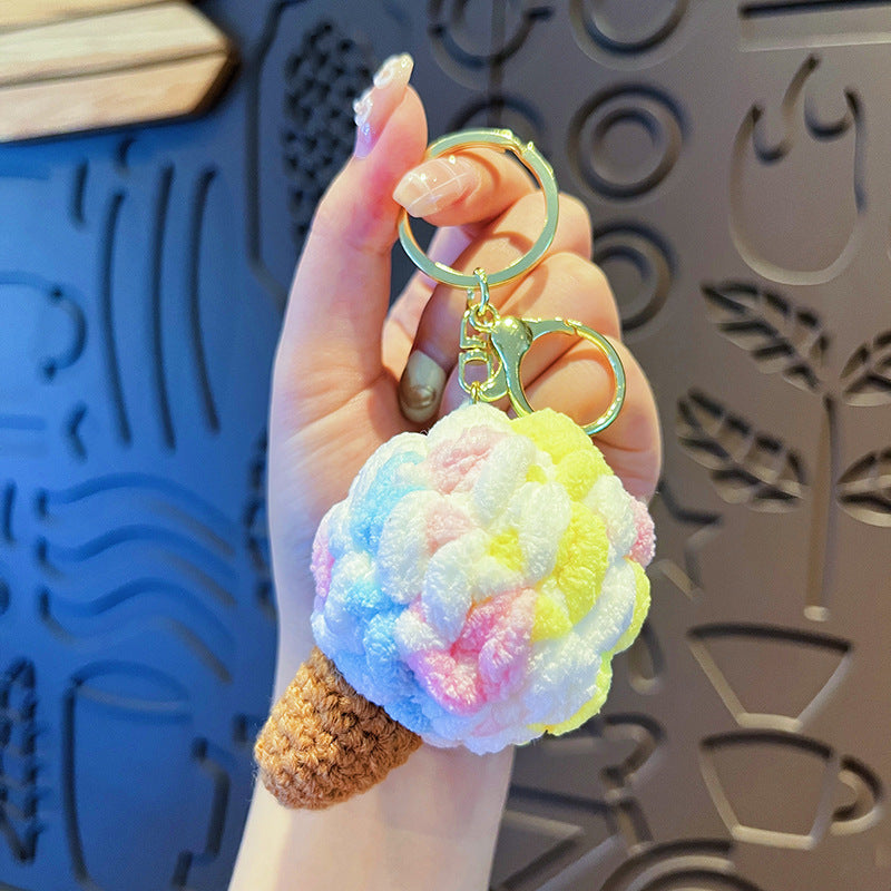 Hand holding one pastel tie-dye plush ice cream cone keychain with brown crochet cone and gold keyring.