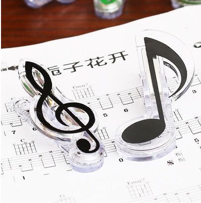 Two clear plastic clips shaped like a treble clef and an eighth note with black insets, on sheet music.