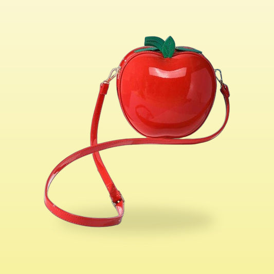 Glossy red apple crossbody bag with a green leaf and long red strap on a butter yellow background